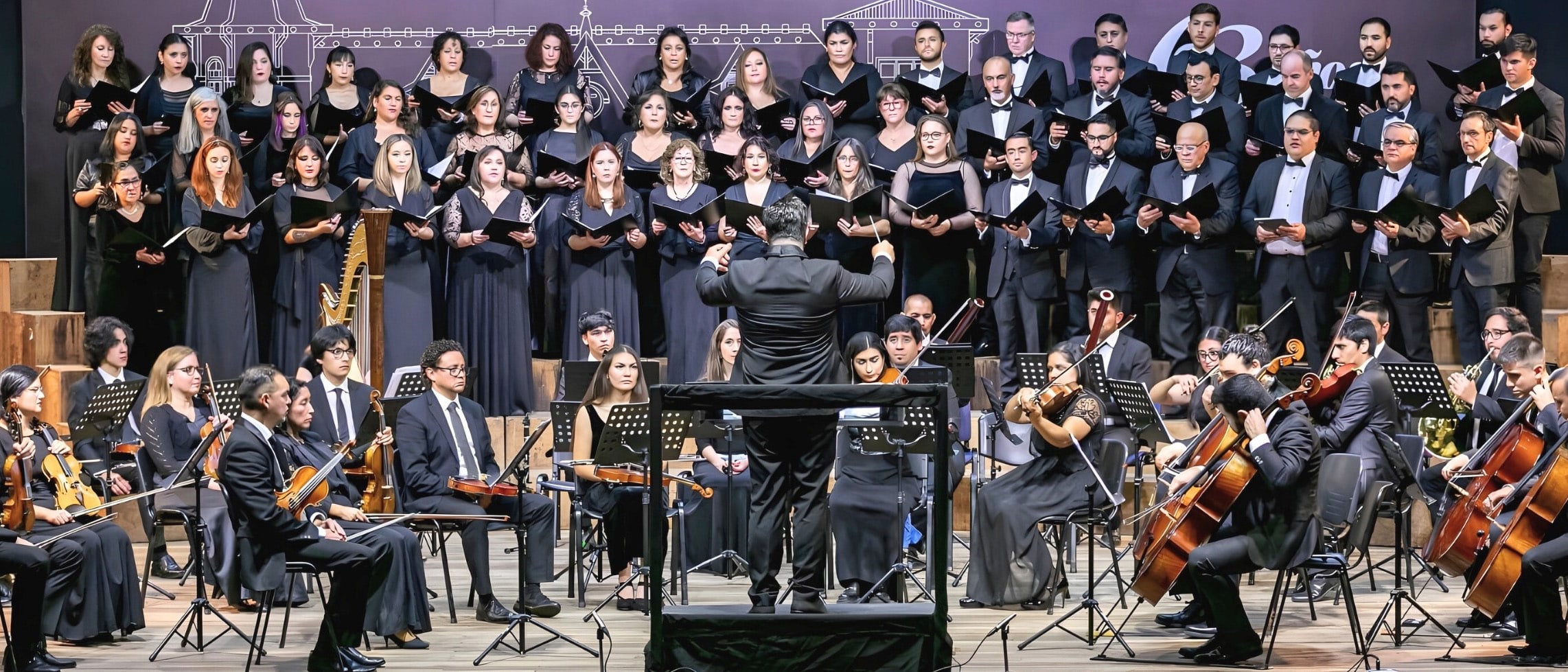 Orquesta sinfónica con coro interpretando música de Queen en el espectáculo Queen Sinfónico bajo la dirección de un maestro en concierto en vivo