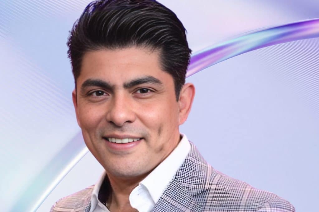 Víctor García en retrato sonriente con saco claro sobre fondo moderno, imagen atractiva ideal para contratación en eventos corporativos y privados